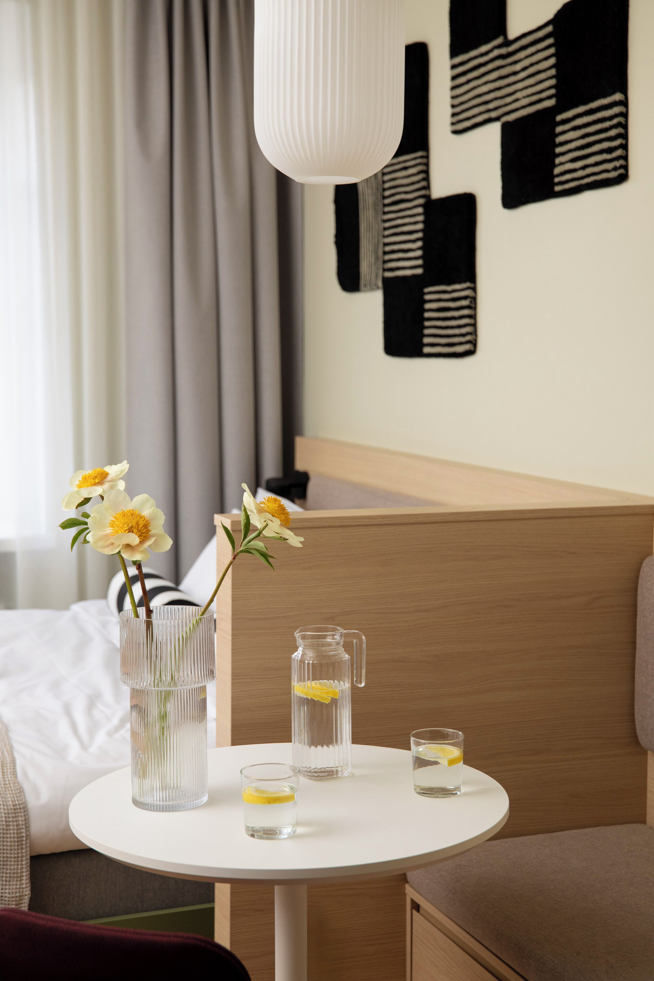 A hotel room with a round table, a vase with flowers, and a pitcher of water.
