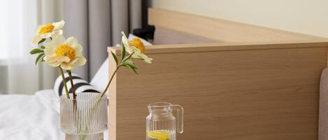 A hotel room with a round table, a vase with flowers, and a pitcher of water.