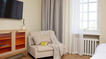 A room with a sofa, a cabinet with glass doors, a radiator, and a window with curtains.