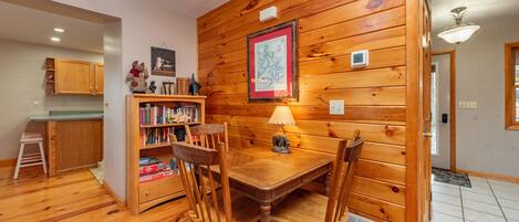 Un coin repas aux murs lambrés, avec une table et des chaises, une bibliothèque et une carte accrochée au mur.