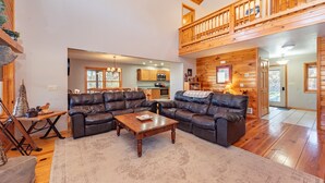 A spacious living room with leather sofas, a wooden coffee table, and a view of the kitchen and upper level.