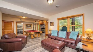 A spacious living room with a pool table, leather sofas, and a fireplace.