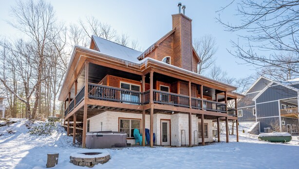 A two-story log cabin with a balcony, a fireplace, and a snow-covered yard.