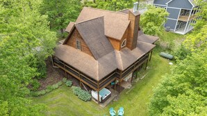 A large, two-story house with a wooden exterior and a sloped roof, surrounded by lush greenery.