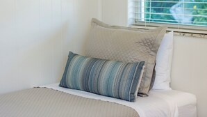 A neatly made bed with a striped pillow and a quilted pillow, set against a white wall with a window in the background.