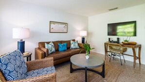 A living room with a brown leather sofa, a blue patterned armchair, a round coffee table, and a TV on a wooden stand.