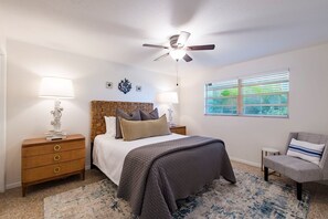 A bedroom with a bed, nightstands, a chair, a ceiling fan, and a window with blinds. - Barefoot Mermaid 1, steps to the beach (Anna Maria)