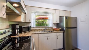 A compact kitchen with a stainless steel refrigerator, a microwave, an oven, and a coffee maker.