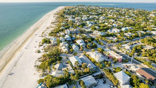 An aerial view of a coastal residential area with houses, a beach, and a clear view of the ocean.
