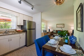 A modern kitchen with a stainless steel refrigerator, a dining area with blue chairs, and a living room with a sofa and a lamp. - Barefoot Mermaid 1, steps to the beach (Anna Maria)