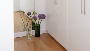 A hallway with white cabinets and a mirror reflecting the room. There are two vases with flowers on the floor. - Bob W London Tower Hill  - Residences (London)