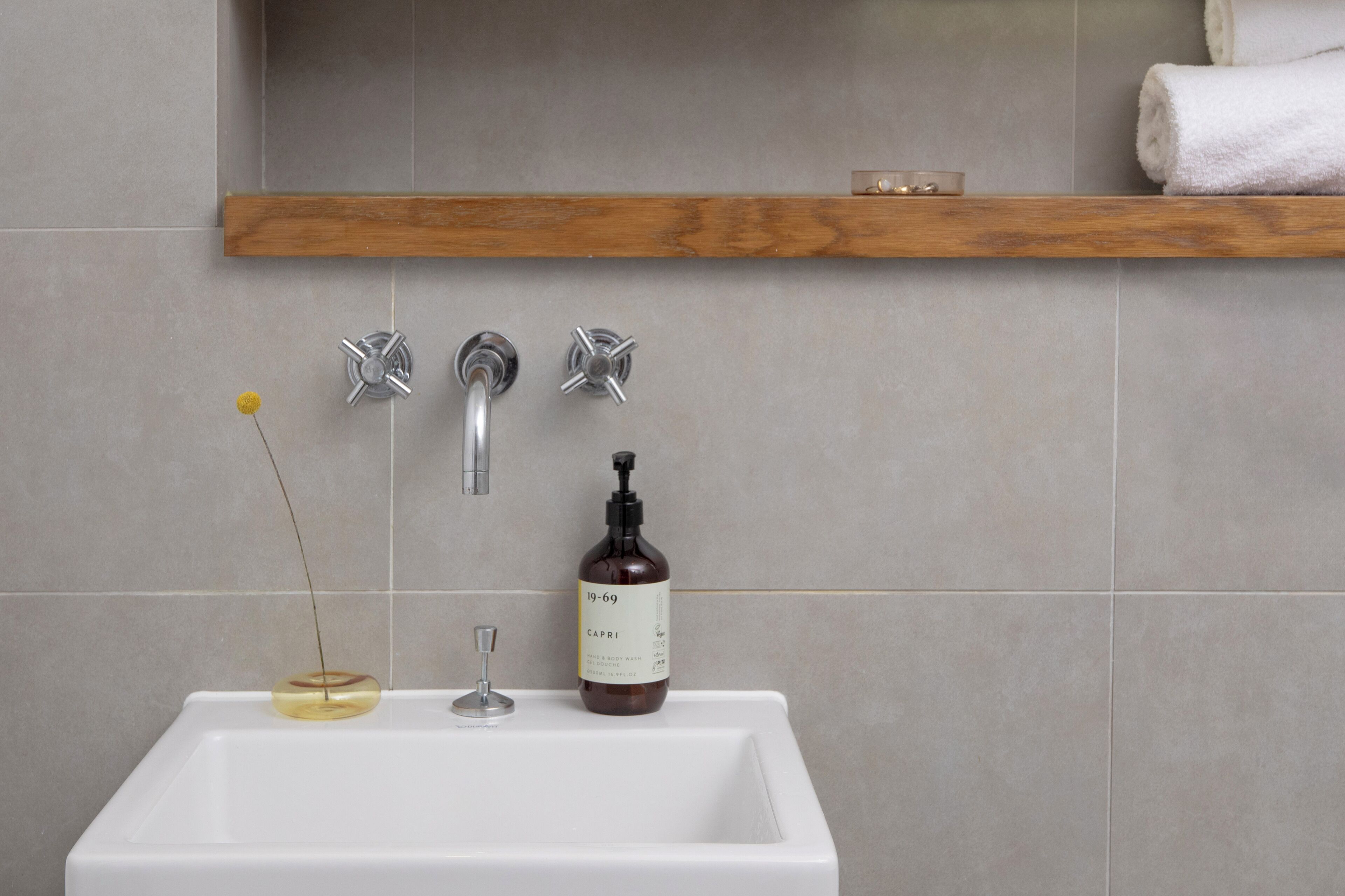 A bathroom sink with a bottle of liquid soap, a glass, and a yellow object on the counter.