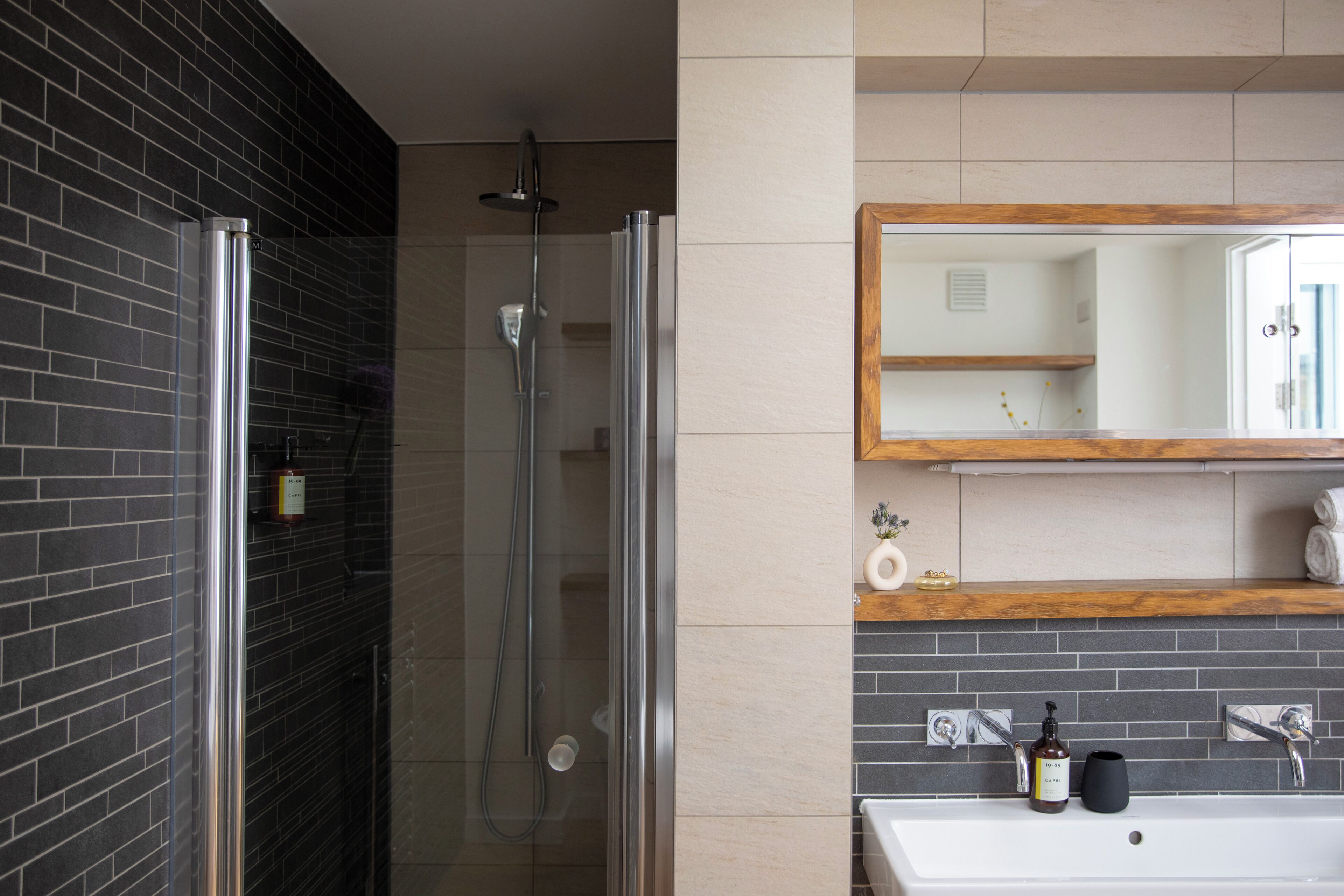 Un bagno moderno con doccia vetro, lavandino bianco e ripiano in legno con articoli da toilette.