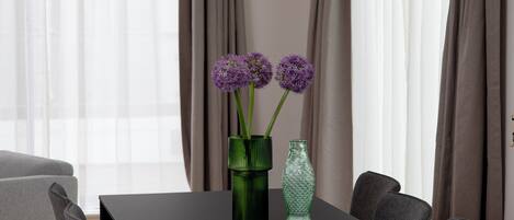 Ein moderner Essbereich mit einem schwarzen Tisch, sechs grauen Stühlen und einer Vase mit violetten Blumen.