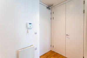 Un pasillo con pared blanca, un termostato, un interruptor de luz y suelo de madera.