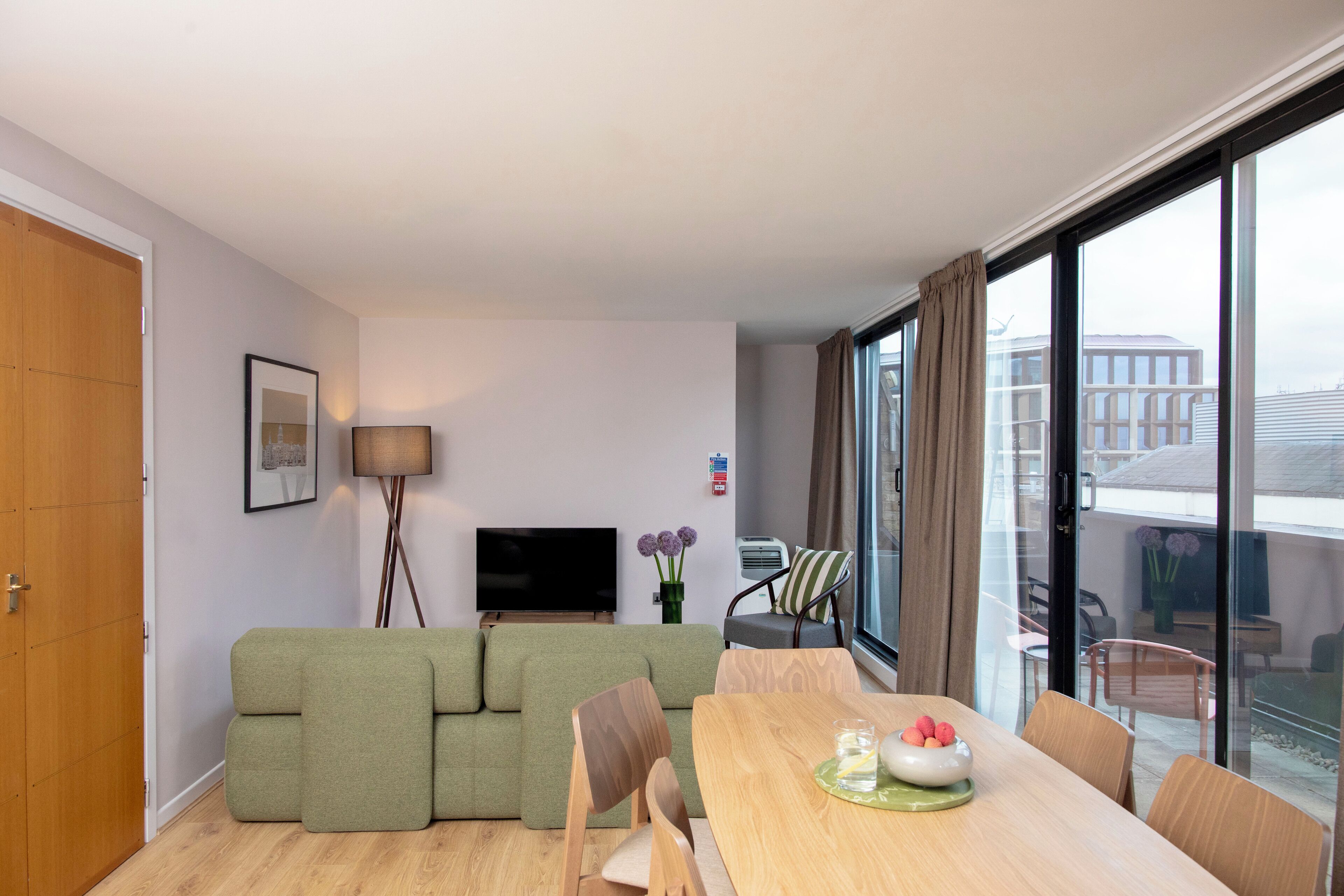 A modern living room with a green sofa, a wooden dining table, and a flat-screen TV.