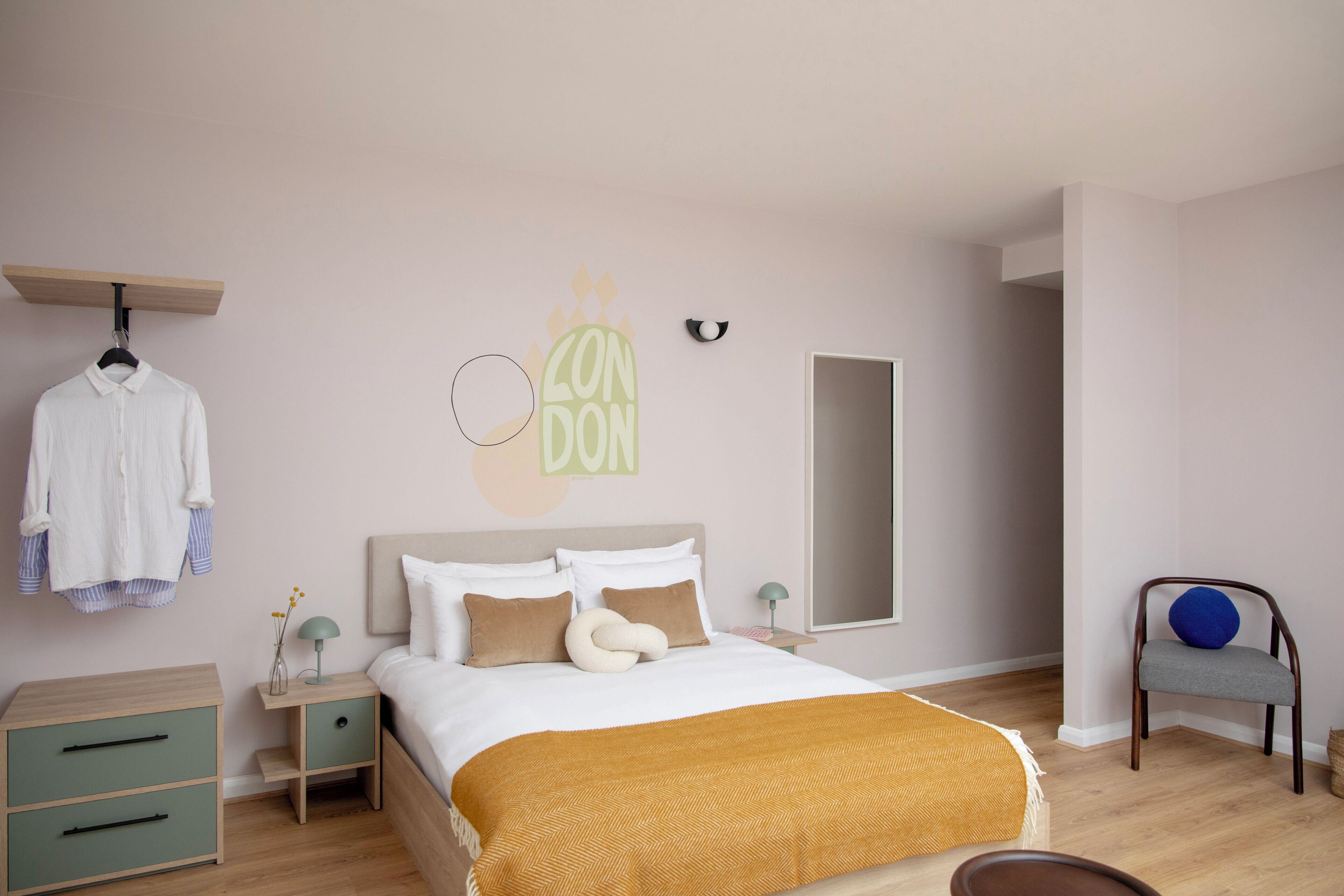 A bedroom with a bed, a nightstand, a dresser, a chair, and a wall with a circular decoration and the word "LONDON".