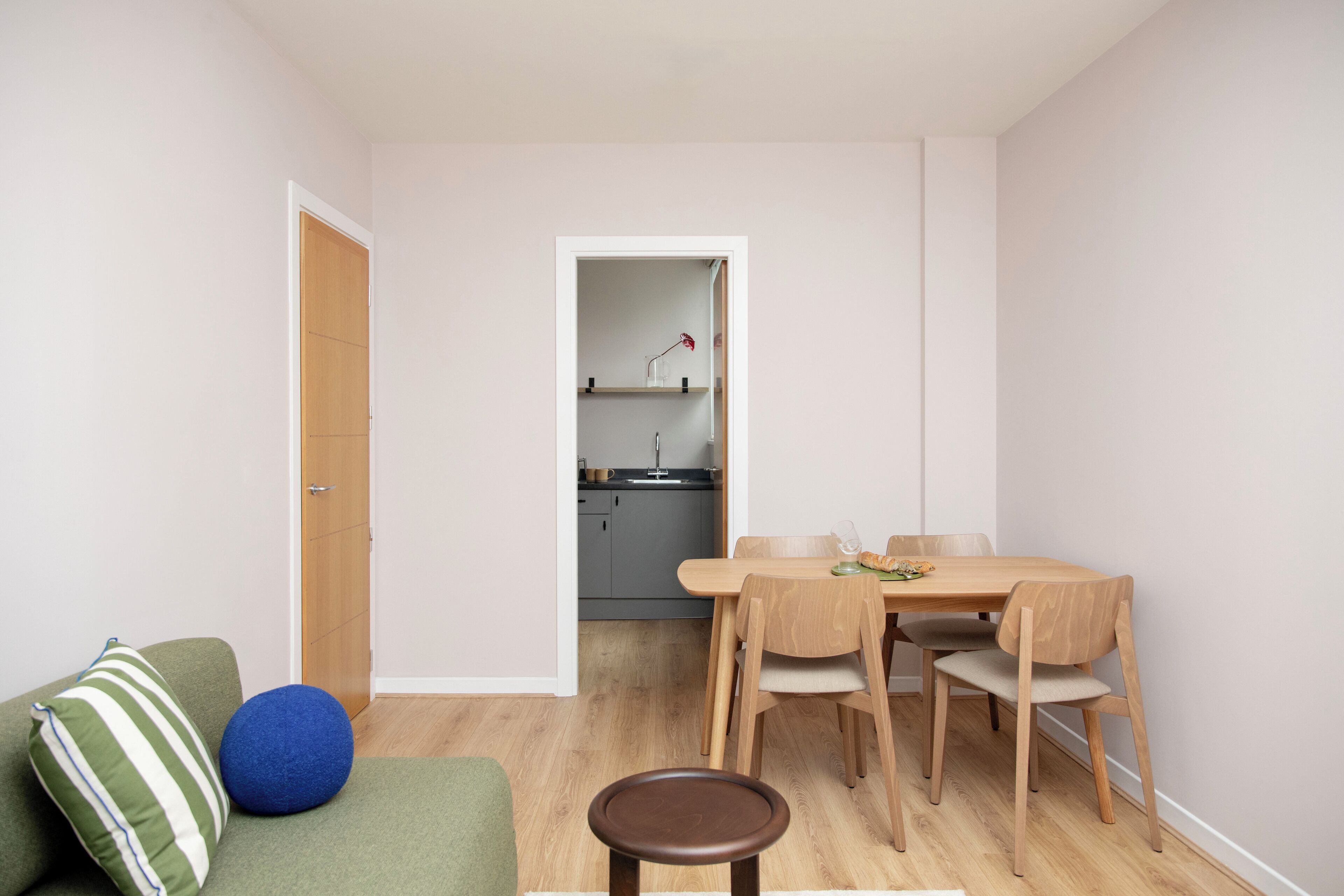 Un espacio habitable compacto con zona de comedor, una cocina al fondo y un sofá verde con cojín a rayas.