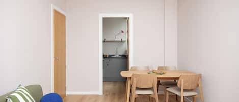 Un espacio habitable compacto con zona de comedor, una cocina al fondo y un sofá verde con cojín a rayas.