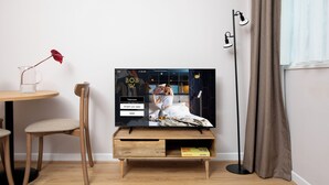 A modern living room with a television on a wooden stand, a small table with a vase, and a floor lamp. - Bob W London St. Paul's (London)