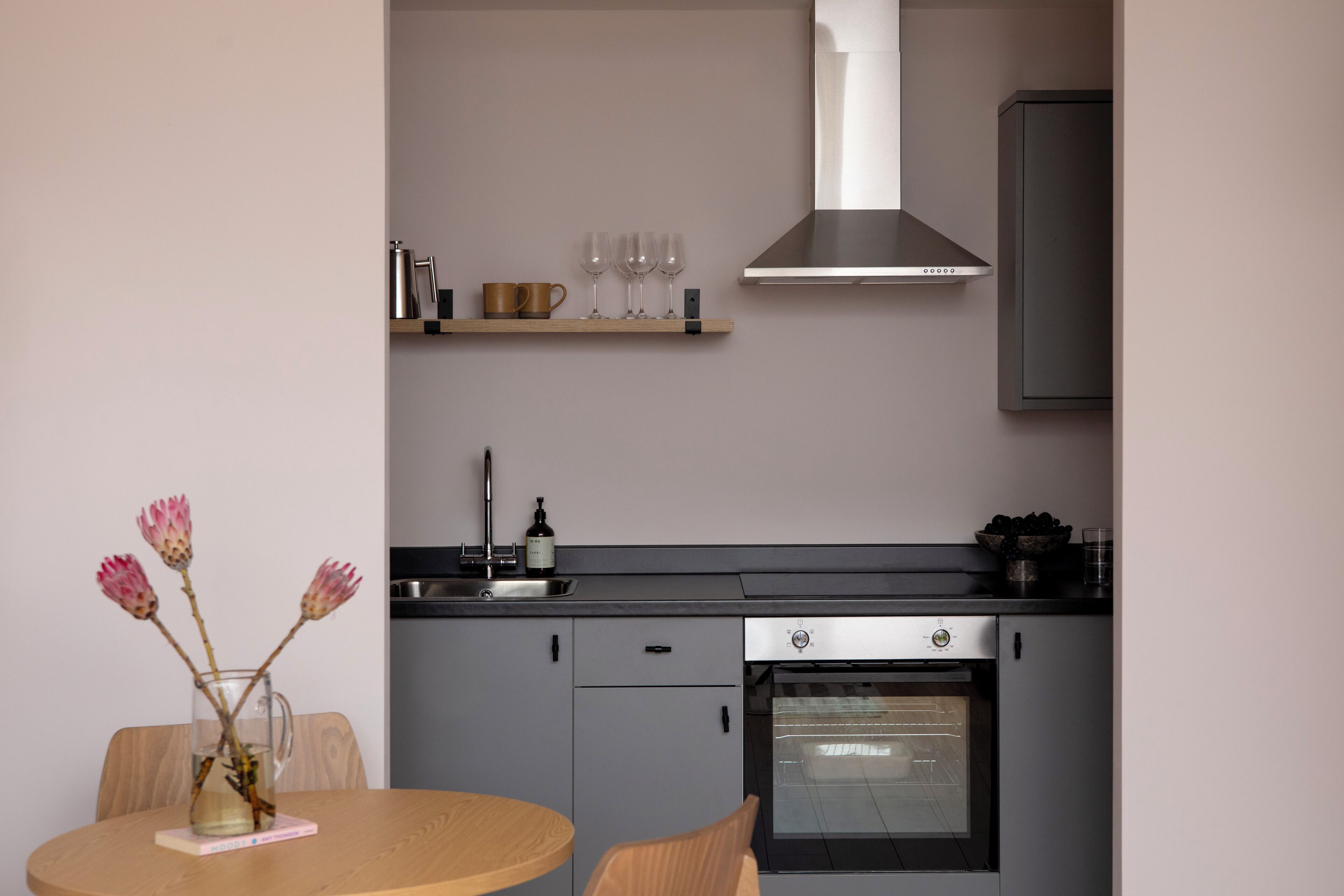 A modern kitchen with grey cabinets, a stainless steel oven, and a black countertop.