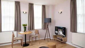 A modern living room with a round table, two chairs, a floor lamp, a television, and a potted plant. - Bob W London St. Paul's (London)