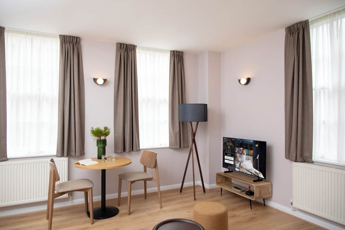 A modern living room with a round table, two chairs, a floor lamp, a television, and a potted plant.
