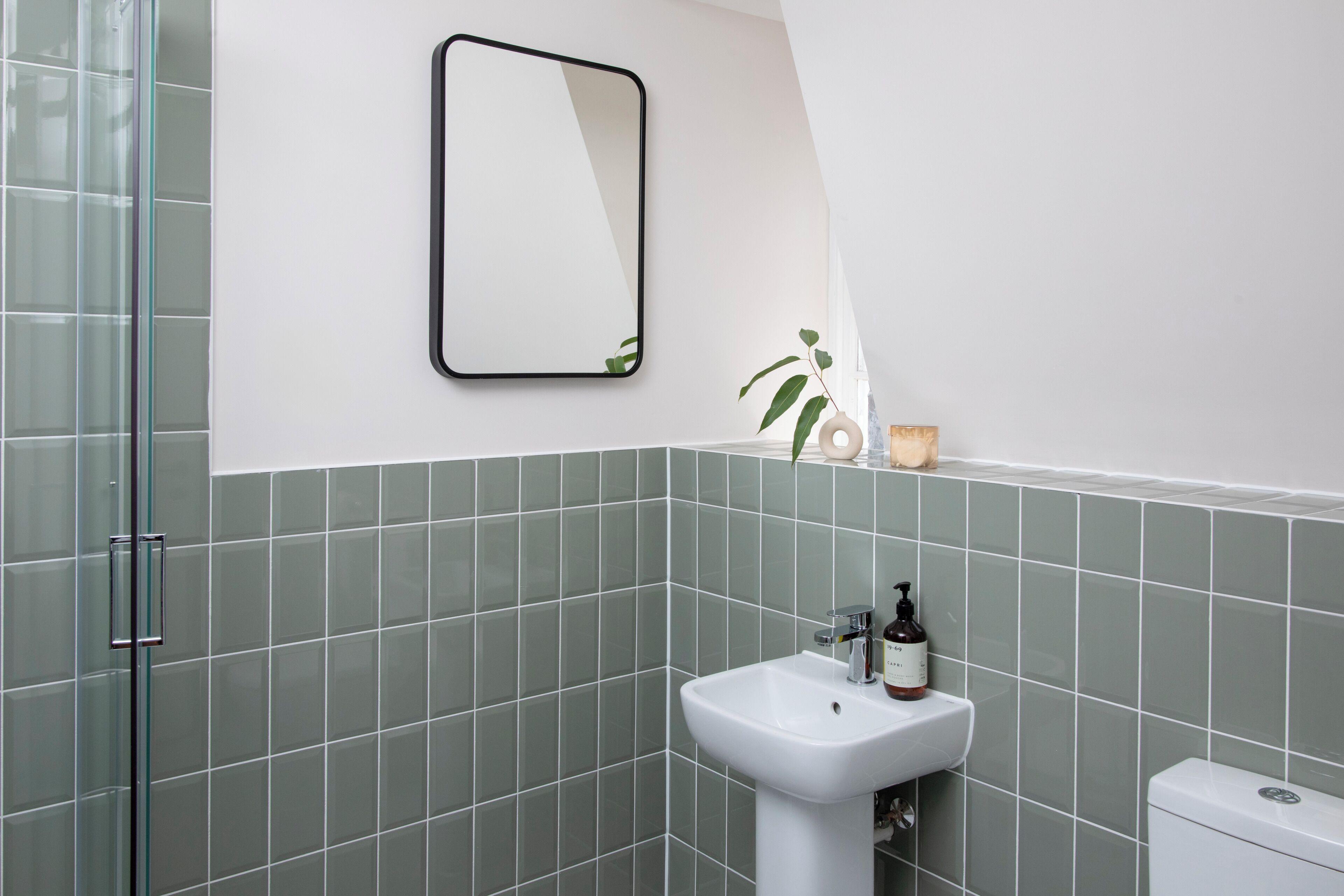 A bathroom with a glass shower enclosure, a white sink with a soap dispenser, and a toilet.