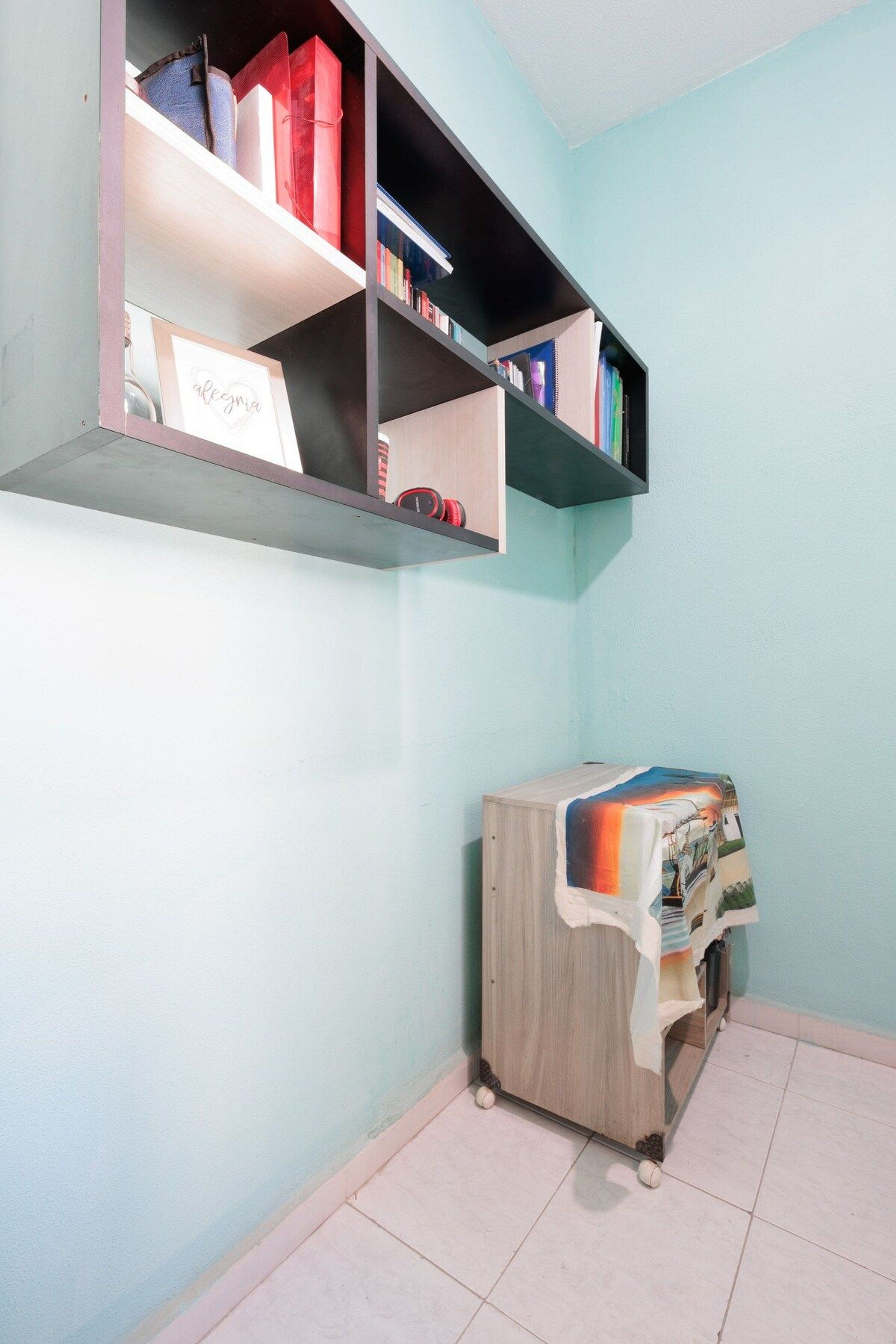 A room with a light blue wall, a bookshelf with various books, and a wooden cabinet with a colorful cover.