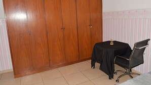Une pièce comprenant une armoire en bois, une petite table recouverte d’une nappe noire et un fauteuil de bureau noir.