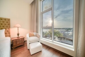 Ein Hotelzimmer mit großem Fenster, einem Bett, einem Nachttisch, einer Lampe und einem Sessel.