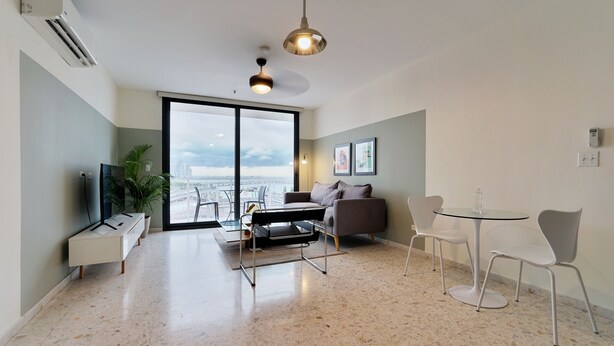 A modern living room with a sofa, a coffee table, a TV, and a dining area with chairs and a table. - La Moderna Downtown Nights by Wynwood (Panama City)