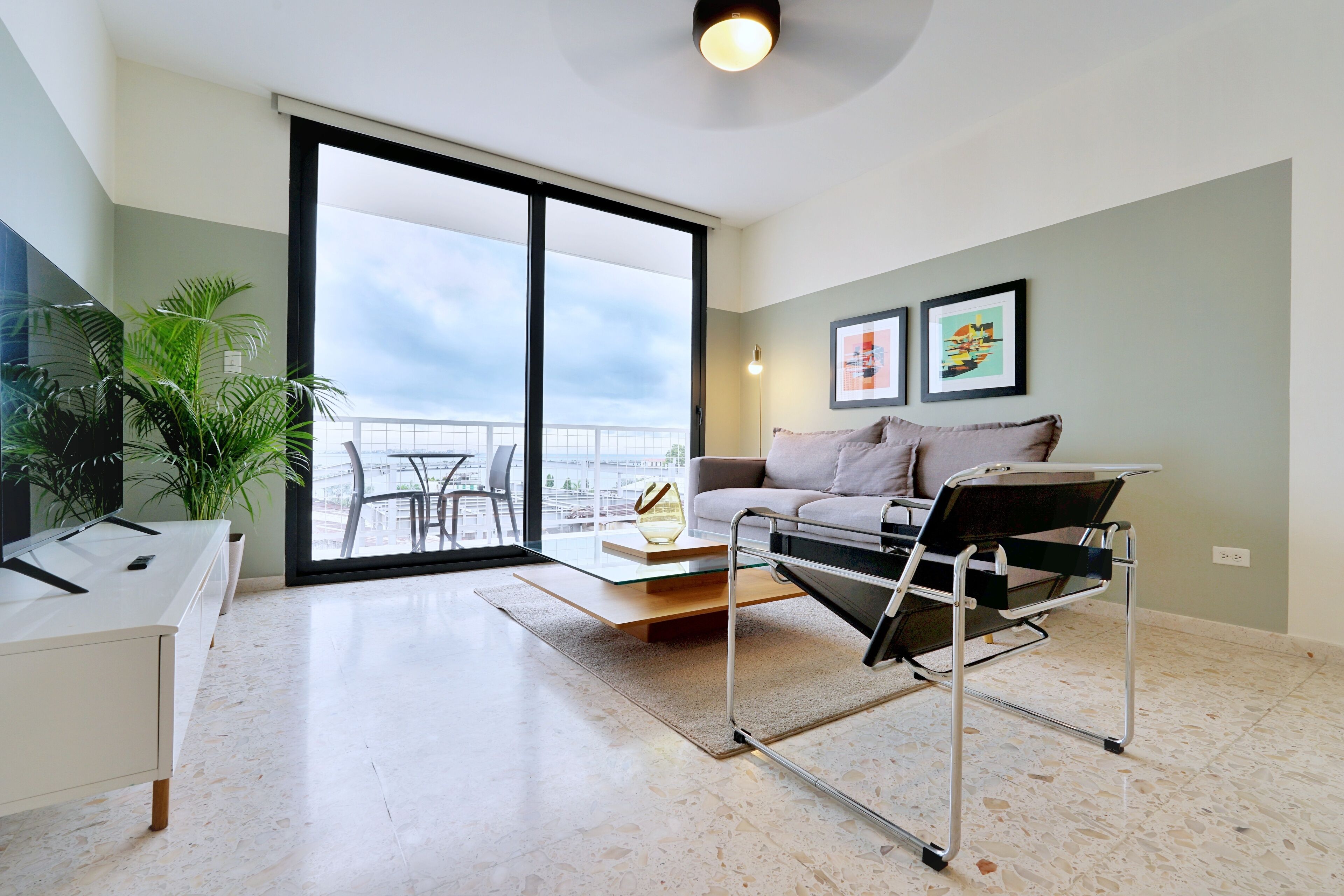 A modern living room with a sofa, a coffee table, and a side table. There is a large window with a view of the city.