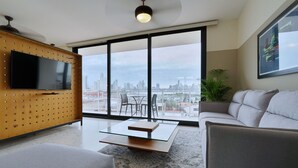 A modern living room with a large TV, a glass coffee table, and a sofa. There is a city view through large windows. - La Moderna Downtown Nights by Wynwood (Panama City)