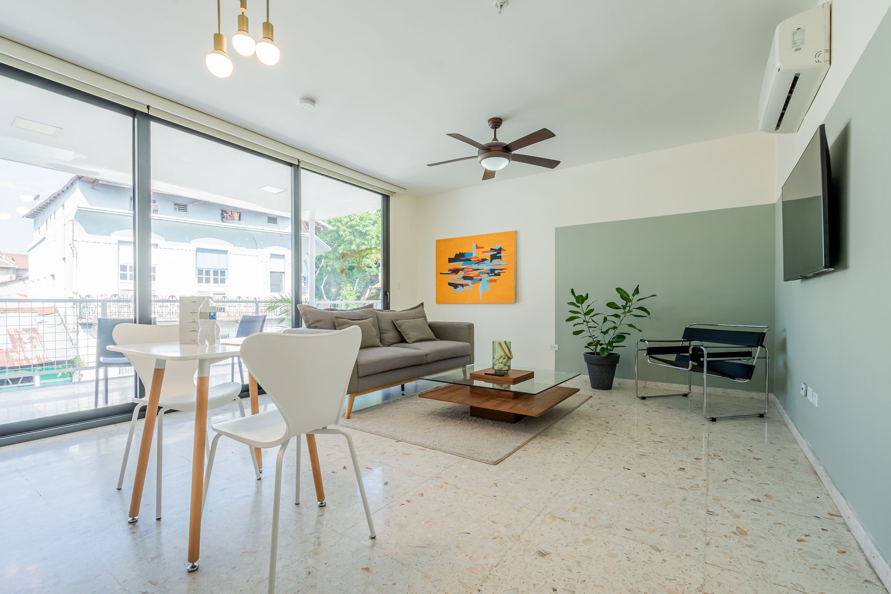 A modern living room with a sofa, chairs, a coffee table, a TV, and a large window.