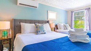 Habitación de hotel con cama, mesita de noche, aire acondicionado, ventana con cortinas y vistas al exterior.