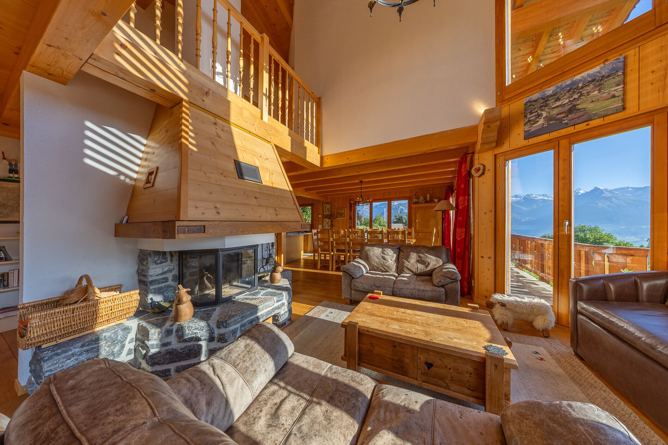 Un amplio salón con chimenea, muebles de madera y ventanas grandes con vistas a la montaña.