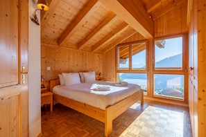 A wooden bedroom with a bed, nightstands, and a window with a view. - Chalet Vansamis, views & sauna (Haute-Nendaz)