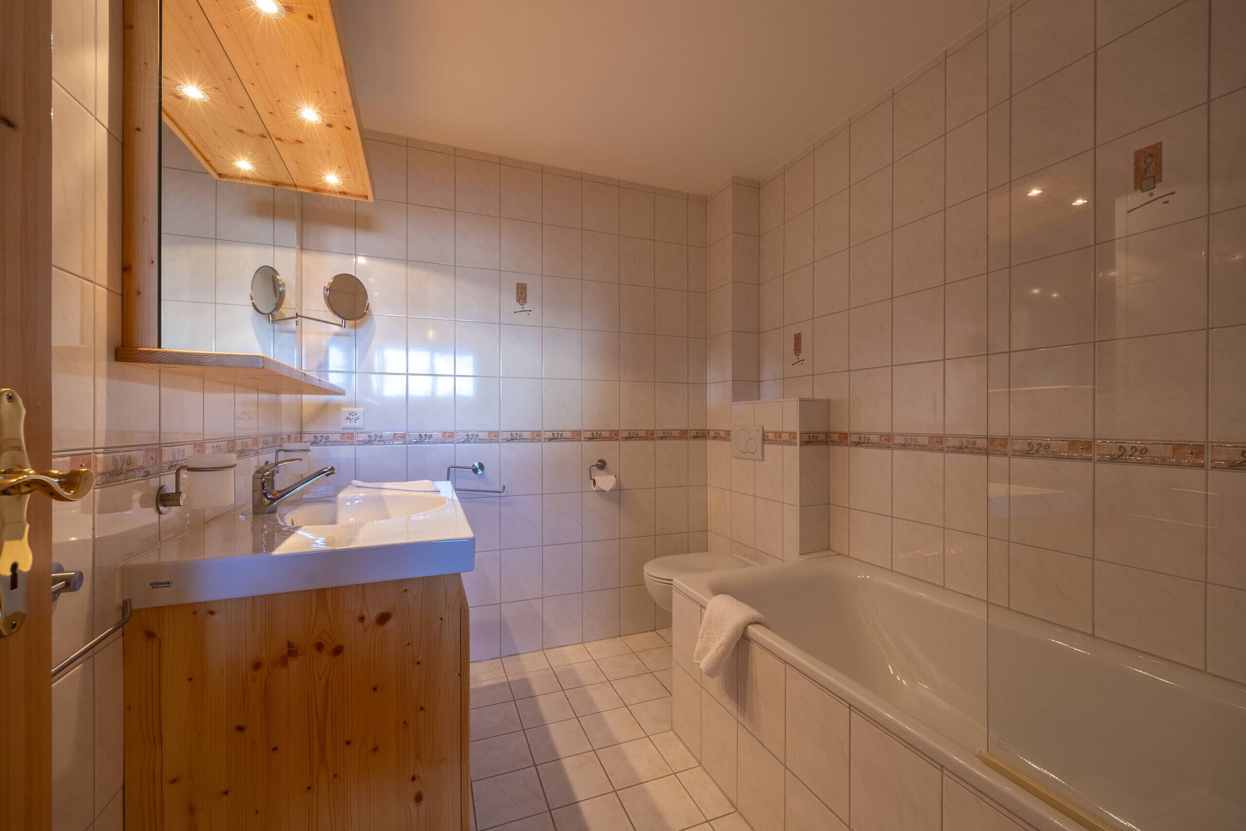 A bathroom with a wooden vanity, a sink, a mirror, a toilet, and a bathtub.