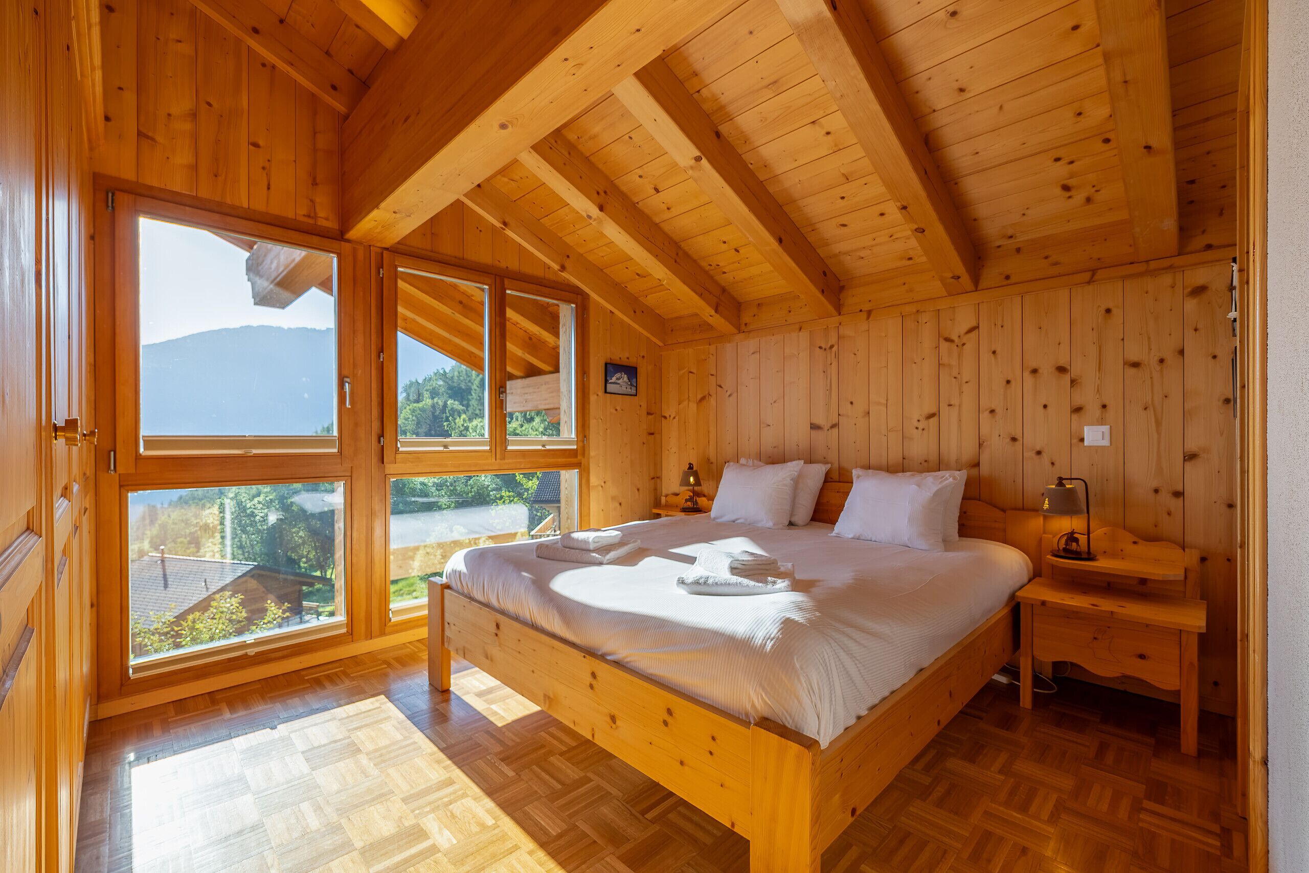 A wooden cabin bedroom with a bed, nightstand, and large windows.
