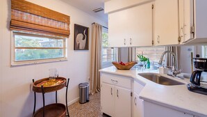 A compact kitchen with white cabinets, a sink, and a window with blinds. - Barefoot Mermaid 4, steps to the beach (Anna Maria)
