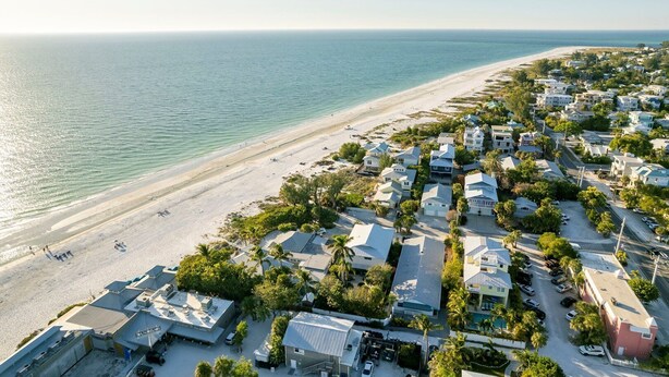 An aerial view of a coastal residential area with houses, a beach, and a clear view of the ocean. - Barefoot Mermaid 4, steps to the beach (Anna Maria)