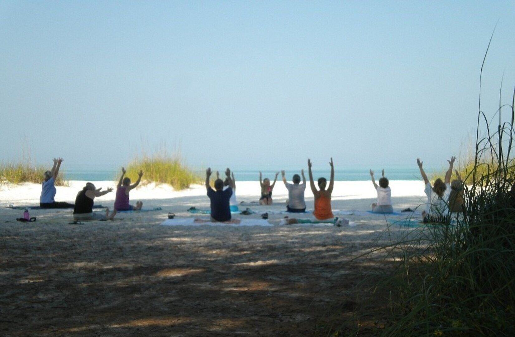 A group of people practicing yoga on a beach with the ocean in the background.