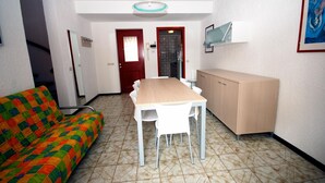 Un espace de vie compact comprenant un canapé, une table à manger avec des chaises, un meuble et une porte donnant sur une douche située à l’arrière-plan.