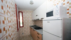 Une cuisine compacte avec des carreaux décoratifs, un réfrigérateur, un four à micro-ondes et une cuisinière à gaz.