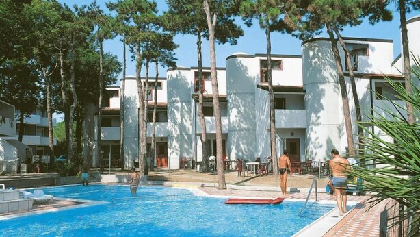 Un espace piscine avec une terrasse carrelée, des chaises longues et un bâtiment doté de balcons en arrière-plan.