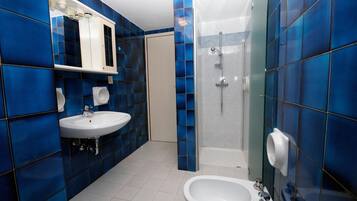 Une salle de bain avec des carreaux bleus, un lavabo blanc, un bidet et un espace douche.