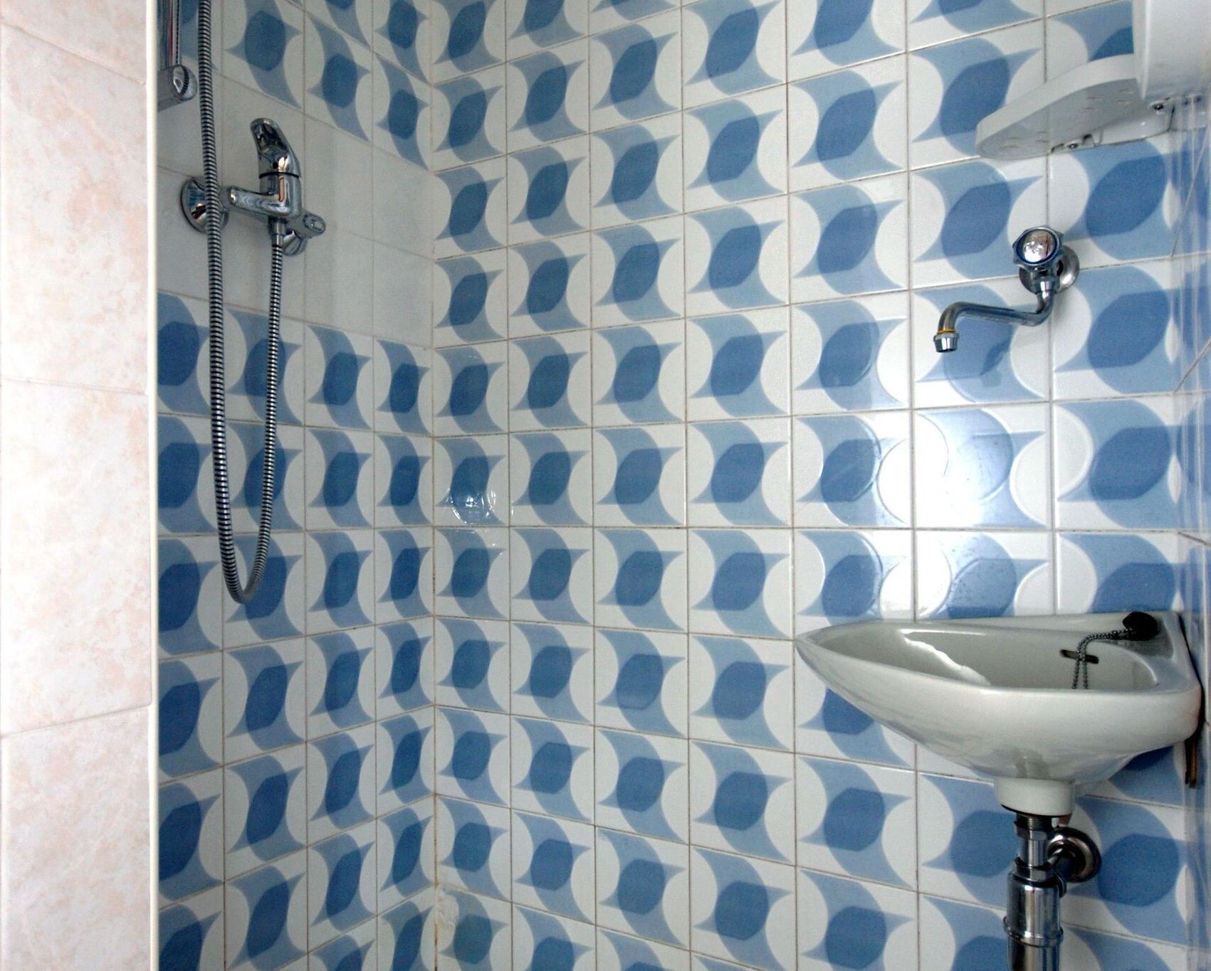 Un baño con pared de azulejos estampados, ducha y lavamanos.