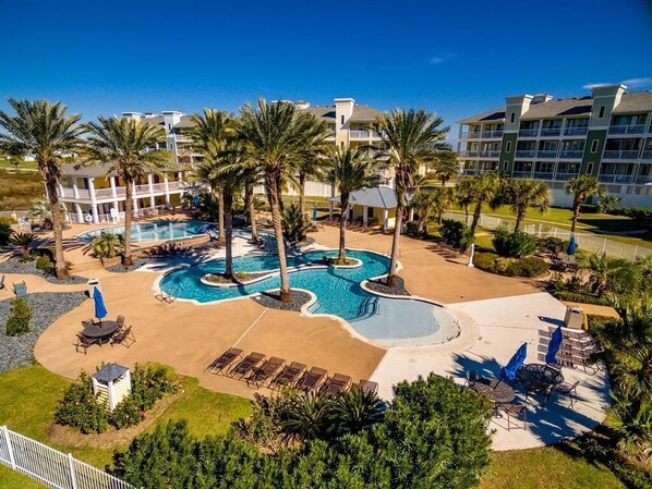 A resort with a central pool, palm trees, and a building with balconies. - Serene-Book 5+ nights get 15% discount. Beach Front. 2BD/2BA-Sleeps 6 (Galveston)