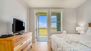 Een slaapkamer met een tv op een houten dressoir, een bed met een bloemenbedekking, een nachtkastje met een lamp en een balkon met uitzicht.